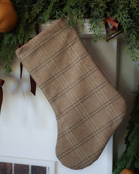 HACKNER HOME handmade caramel wool plaid Christmas stocking in Boho design, featuring warm brown tones and textured heritage plaid fabric, styled beneath evergreen garland.