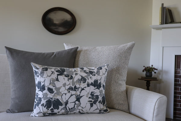 Gray and black designer pillow covers styled on a cream sofa, featuring a floral lumbar pillow layered with solid charcoal gray and textured neutral decorative throw pillows by HACKNER HOME.