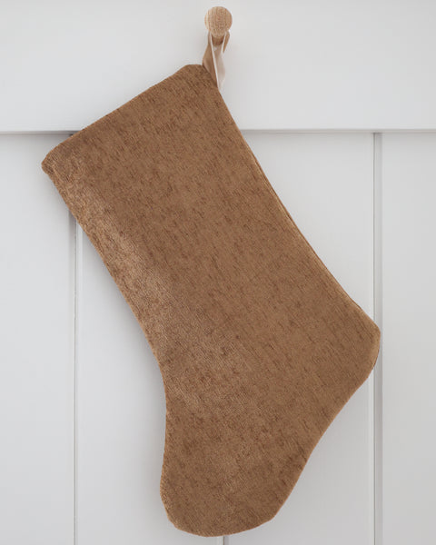 Praline Textured Stocking, Boho Design Christmas stocking in warm caramel textured fabric with deeper brown slubs and a sand velvet hook, hanging from a wooden peg on a white paneled wall
