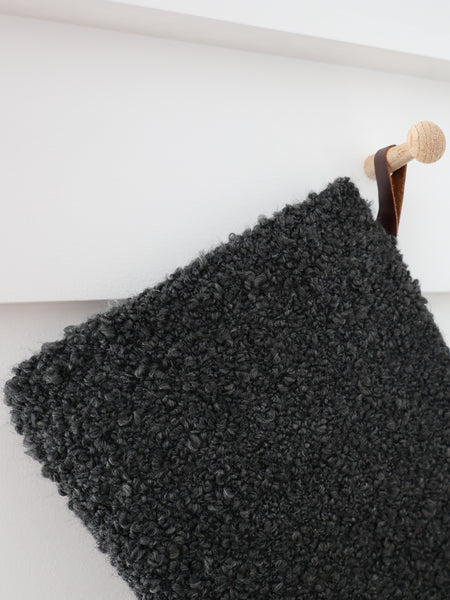 Close-up detail of Charcoal Boucle Stocking showing dense, curly charcoal boucle texture and a dark brown hanging loop on a wooden peg