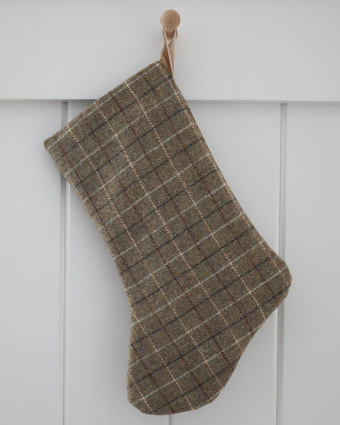 Deeply Green Plaid Wool Stocking, Boho Design Christmas stocking in deep green wool with fine cream, brown and charcoal plaid lines and a sand velvet loop, hanging from a wooden peg on a white paneled wall