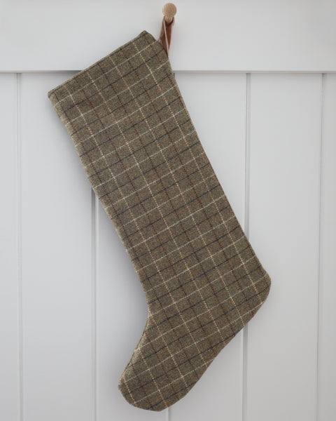 Deeply Green Plaid Wool Stocking, Large Design Christmas stocking in deep green wool with fine cream, brown and charcoal plaid lines and a sand velvet loop, hanging from a wooden peg on a white paneled wall