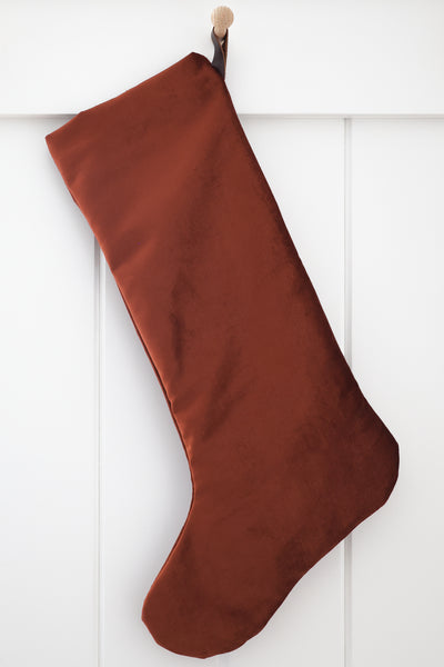 Cider Velvet Stocking, Large Minimal Design tall Christmas stocking in rich rust-terracotta polyester velvet with a dark brown strap hook, hanging from a wooden peg on a white paneled wall