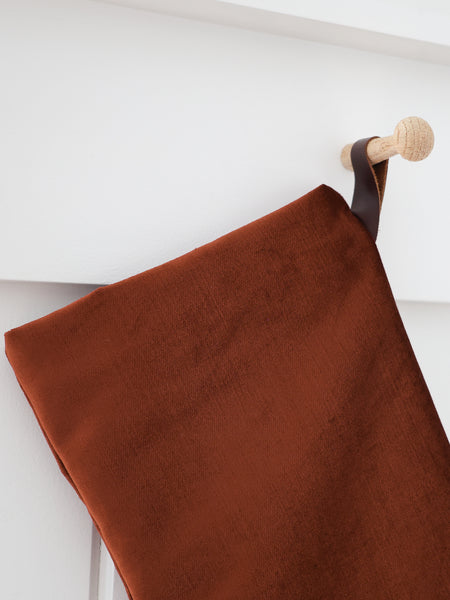 Close-up detail of Cider Velvet Stocking showing soft, dense rust-terracotta velvet and a dark brown strap hook on a wooden peg