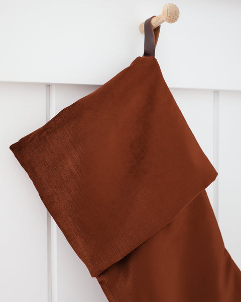 Close-up detail of Cider Velvet Stocking showing the soft, dense rust-terracotta velvet cuff and dark brown strap hook on a wooden peg