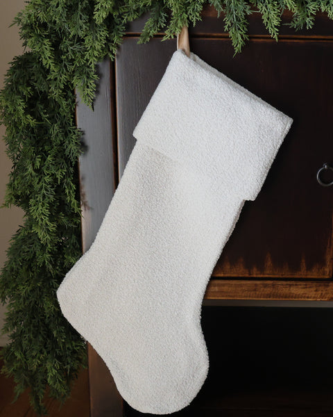 Handmade textured white Christmas stocking with plush woven fabric and traditional folded cuff, displayed with evergreen garland by HACKNER HOME.