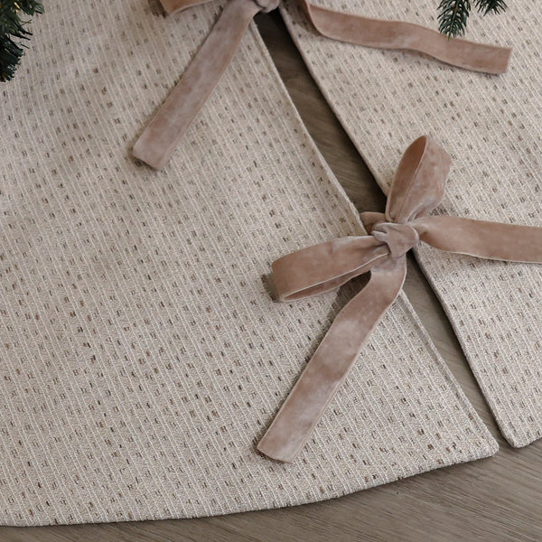 Ivory handmade Christmas tree skirt in textured designer fabric with soft velvet ribbon ties beneath an evergreen Christmas tree