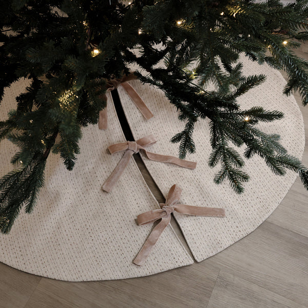 Ivory handmade Christmas tree skirt in textured designer fabric with soft velvet ribbon ties beneath an evergreen Christmas tree