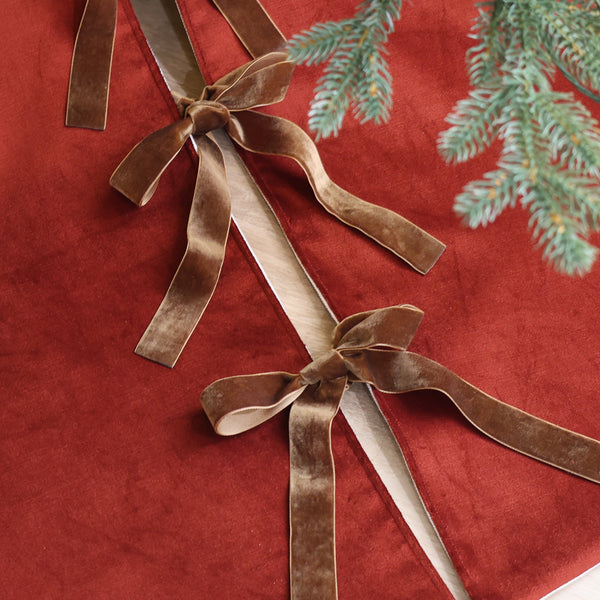 Luxury red velvet Christmas tree skirt handmade in the USA with warm brown velvet ribbon bows beneath a lighted evergreen Christmas tree.