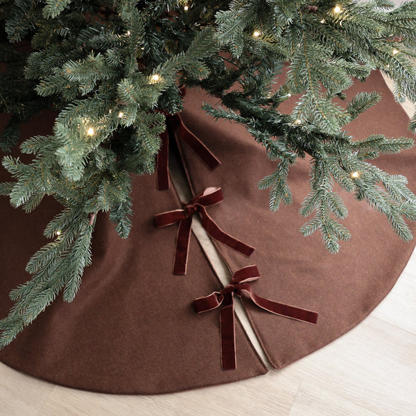 Pumpernickel brown wool blend handmade Christmas tree skirt with velvet ribbon ties under an evergreen Christmas tree