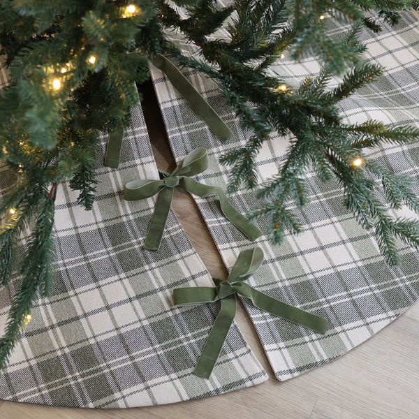 Sage green and ivory plaid handmade Christmas tree skirt with green velvet ribbon bows beneath an evergreen Christmas tree.