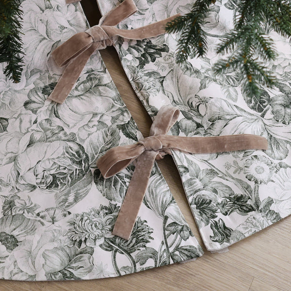 Vintage floral handmade Christmas tree skirt in ivory designer cotton with botanical flower print and taupe velvet ribbon bows beneath an evergreen tree.