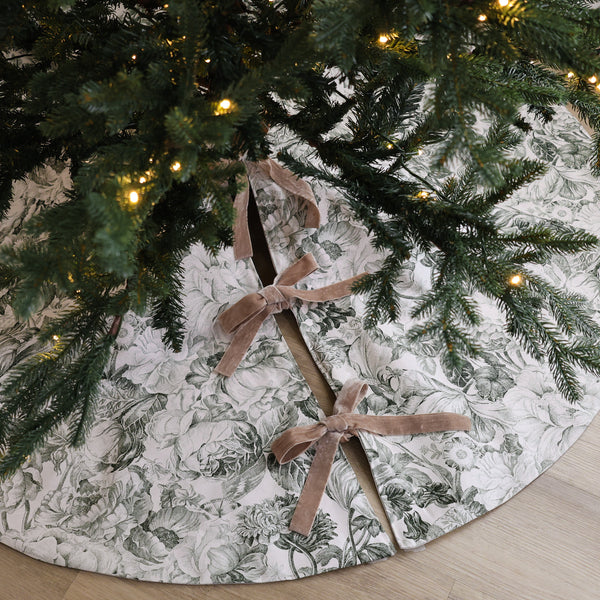 Vintage floral handmade Christmas tree skirt in ivory designer cotton with botanical flower print and taupe velvet ribbon bows beneath an evergreen tree.