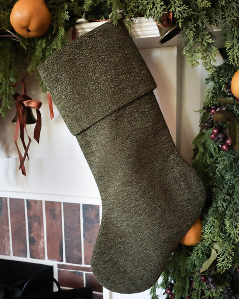 HACKNER HOME handmade dark olive green Christmas stocking with folded cuff, richly textured designer fabric, and subtle golden accents, styled with traditional Christmas greenery.