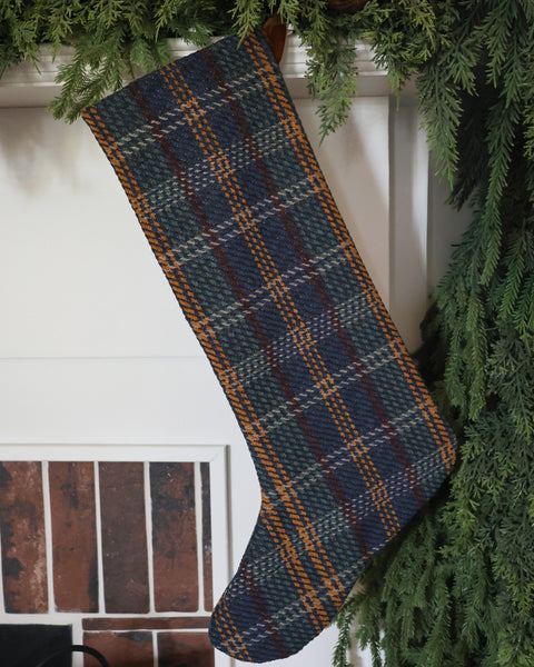 HACKNER HOME handmade Blue Tartan Plaid Christmas Stocking in Large Minimal Design, featuring navy blue, forest green, and golden brown plaid, styled with evergreen garland on a traditional Christmas mantel.