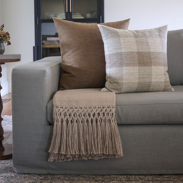 HACKNER HOME brown and neutral designer pillow covers styled on a sofa with a textured fringed throw blanket, creating a warm, layered luxury living room.