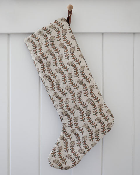 Willow Stem Linen Block Print Stocking, Large Design linen Christmas stocking with hand-printed chestnut brown stems, sage leaves and pale green buds on natural flax and a rust velvet hook, hanging from a wooden peg on a white paneled wall