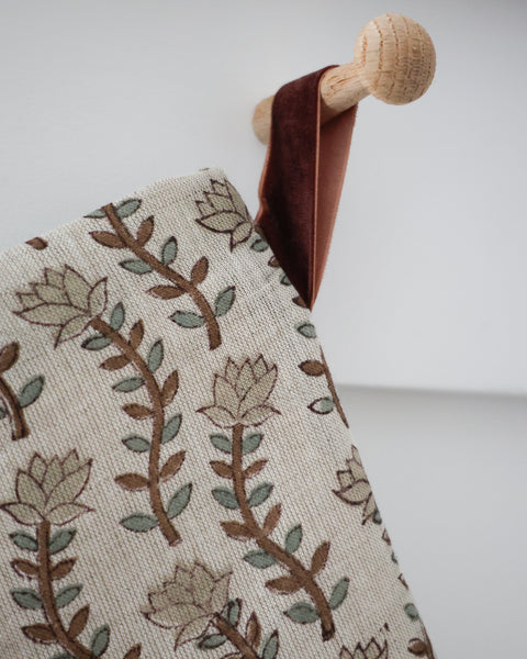 Close-up detail of Willow Stem Linen Block Print Stocking showing block-printed brown stems, sage leaves and pale buds on natural linen with a rust velvet hook on a wooden peg