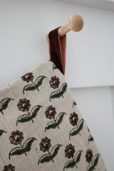 Close-up detail of Vintage Rose Block Print Stocking showing block-printed burgundy blooms and olive leaves on natural linen with a rust velvet hook on a wooden peg