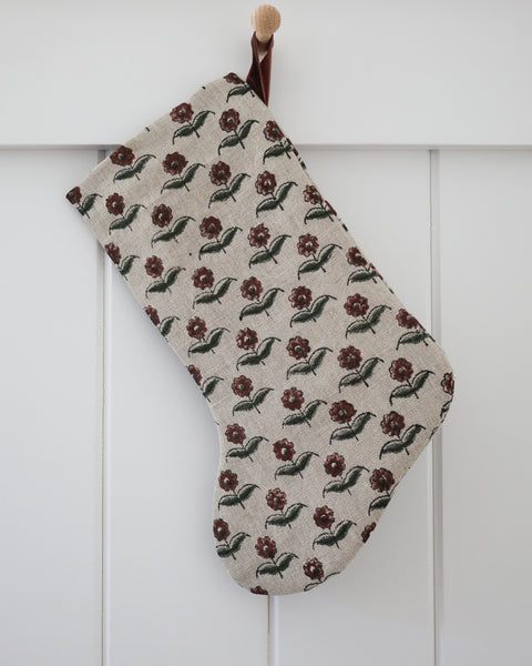 Vintage Rose Block Print Stocking, Boho Design linen Christmas stocking with hand-printed deep burgundy blooms and olive green leaves on natural flax and a rust velvet hook, hanging from a wooden peg on a white paneled wall