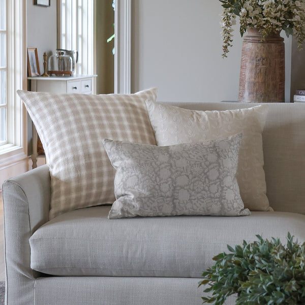 Neutral designer pillow covers styled on a cream sofa, featuring beige plaid, white embroidered botanical and soft gray floral lumbar pillows by HACKNER HOME.