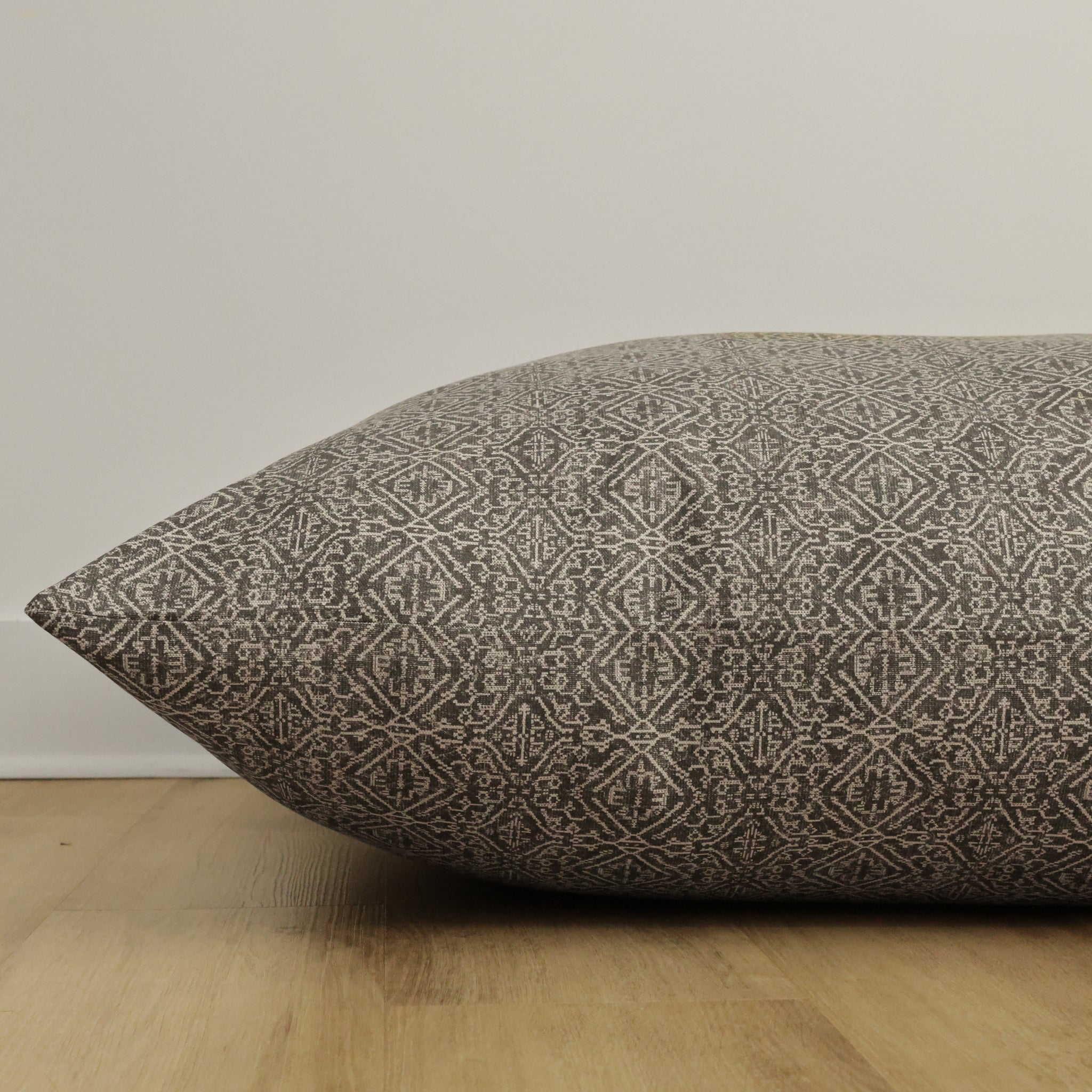 Side view of Hackner Home Acadia floor pillow cover showcasing its intricate geometric woven pattern in neutral tones on a wooden floor background.