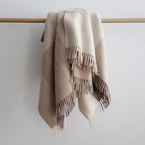 Soft alpaca and sheep wool throw blanket in beige and brown color blocks with fringed edges, draped over a wooden rod.