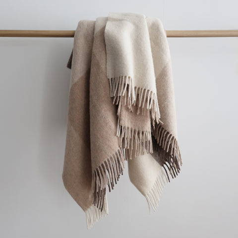 Soft alpaca and sheep wool throw blanket in beige and brown color blocks with fringed edges, draped over a wooden rod.