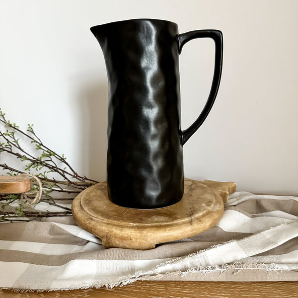 Hackner Home black hand-formed ceramic serving pitcher styled on a wooden board with neutral linen and greenery for a modern farmhouse display.