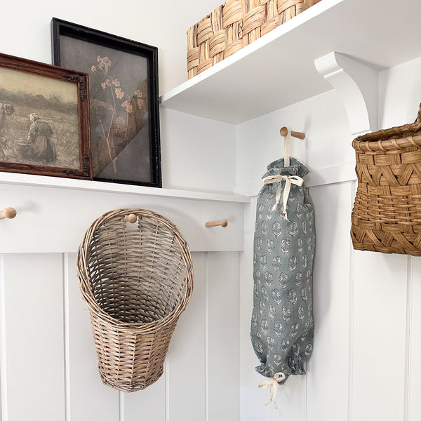 Hackner Home blue linen grocery bag holder with white floral print hanging in a farmhouse laundry room with woven baskets and rustic wall decor.