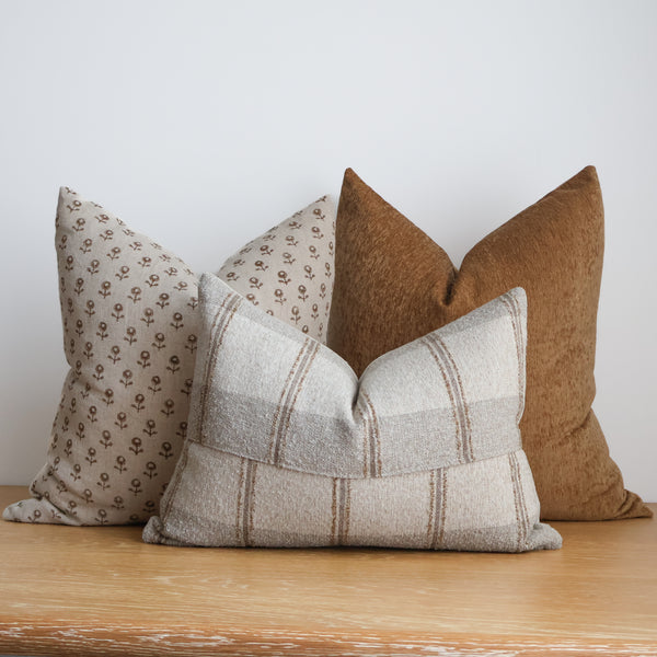 Hackner Home Cottage Ember pillow cover set styled on a wood table, featuring warm brown, beige, and cream tones with floral, solid, and striped patterns.