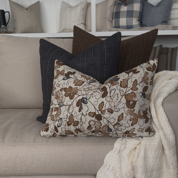 Hackner Home Cottage Harvest pillow cover set styled on beige sofa with cozy knit throw, featuring dark brown, charcoal, and floral patterns for a warm autumn-inspired living room look.