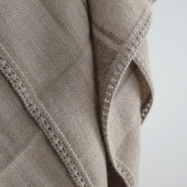 Close-up of soft woven baby alpaca throw blanket in light brown, showing detailed crocheted edge and fine textured weave.