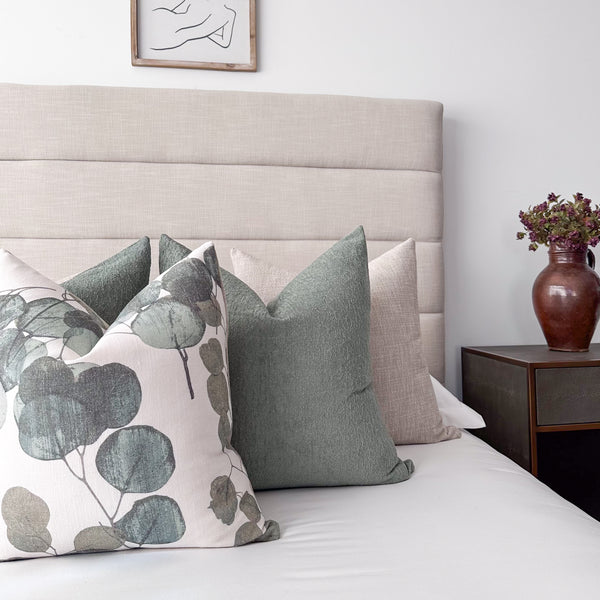 Bedroom styled with Hackner Home Eucalyptus Leaf pillow cover layered with solid green and beige pillows on a neutral upholstered headboard.