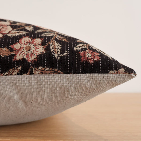 Close-up side view of a pillow cover featuring a floral block print in rose and beige tones on a dark background with a plain beige fabric on the back.