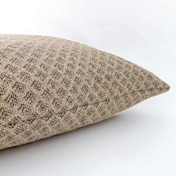 Close-up side view of a beige pillow with a textured diamond weave pattern, displayed against a white background.