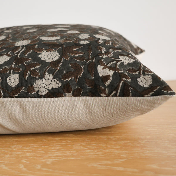 Side view of a pillow with a dark floral block print fabric on top and a natural beige linen backing, resting on a wooden surface.
