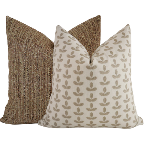 Set of two decorative pillows featuring a brown textured woven cover and a cream pillow with embroidered tan leaf patterns, styled together for a warm fall-inspired look.