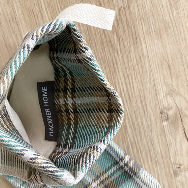 Close-up of the Hackner Home Green Plaid Boho Christmas Stocking showing the top opening, cream cotton loop hanger, and interior label with ‘HACKNER HOME’ tag, highlighting the green, beige, and brown plaid fabric texture.