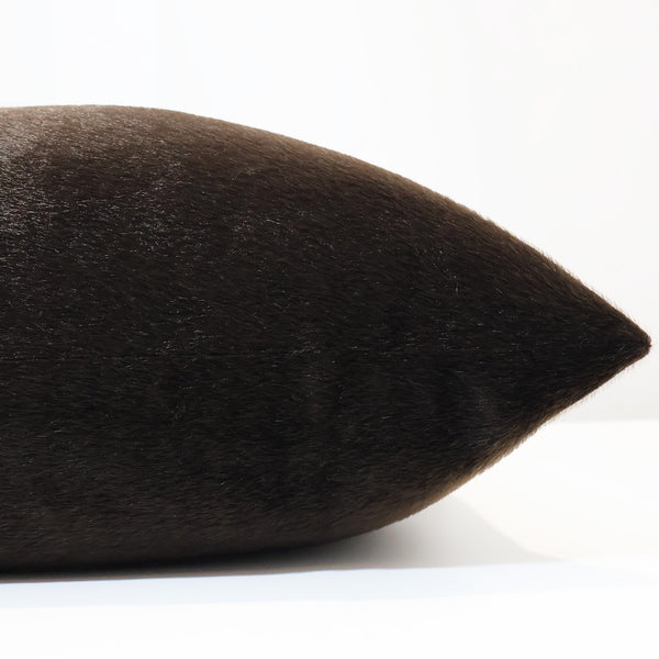 Close-up side view of a dark brown faux fur pillow cover, showing its sleek texture and subtle sheen.