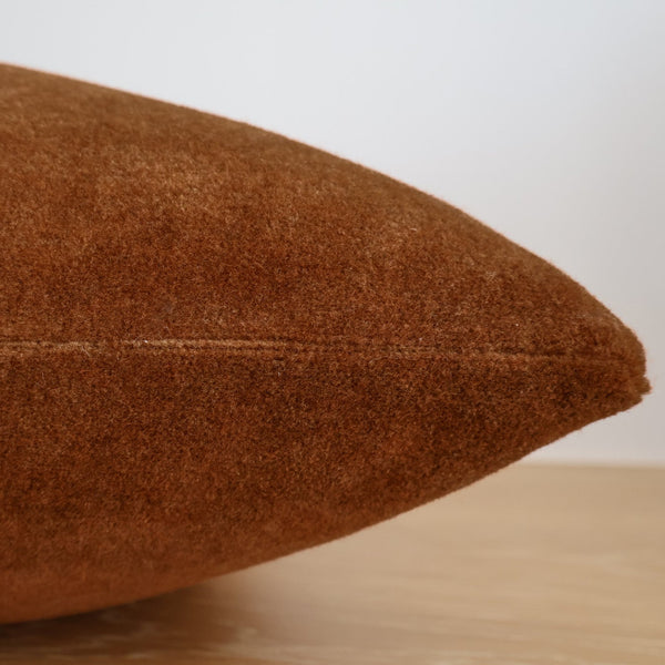 Side view of a rust-colored mohair pillow cover highlighting its soft, fuzzy texture and neatly stitched seam.
