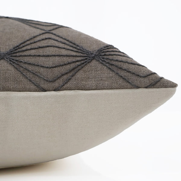 Close-up side view of a brown pillow cover with dark diamond embroidery and a solid light beige backing.
