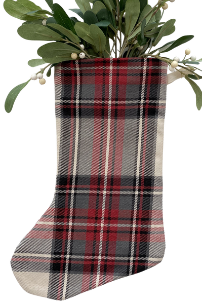 Red, black, and cream plaid Christmas stocking with greenery and white berries arranged inside, displayed on a white background.
