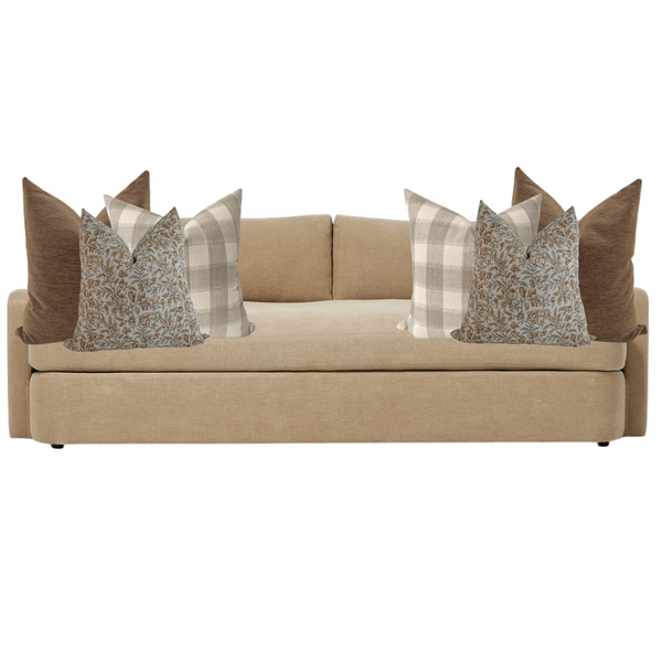 Beige upholstered sofa styled with six decorative pillows in warm earthy tones, including solid brown, neutral plaid, and blue floral block print covers for an inviting autumn-inspired look.