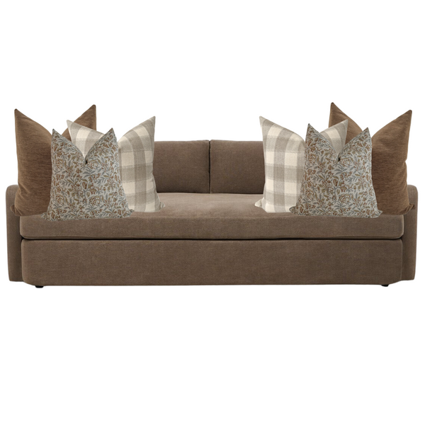 Brown upholstered sofa styled with six decorative pillows in coordinating neutral tones, including solid brown, beige plaid, and floral block print designs.