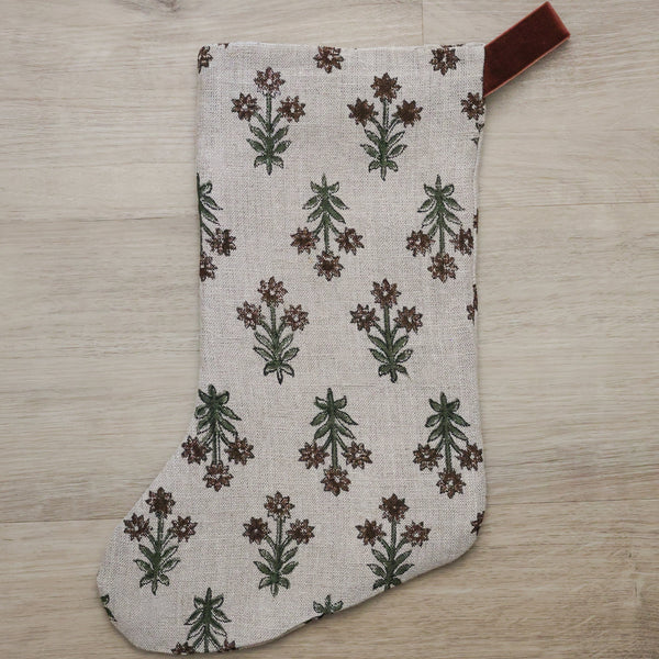 Hackner Home Wood Lily Block Print Christmas Stocking featuring a hand-printed floral design in earthy green and brown tones on a natural linen fabric, accented with a brown velvet hanging loop for a warm, boho-inspired holiday look.