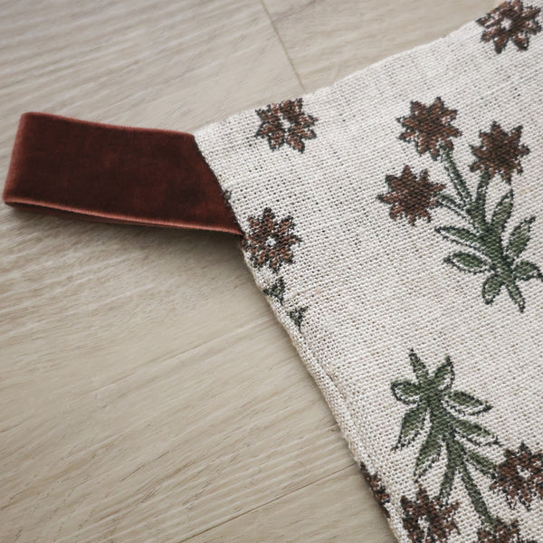 Hackner Home Wood Lily Block Print Christmas Stocking featuring a hand-printed floral design in earthy green and brown tones on a natural linen fabric, accented with a brown velvet hanging loop for a warm, boho-inspired holiday look.